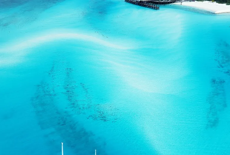 Aerial of a lone sailboat over swirling turquoise sandbanks near a small cay