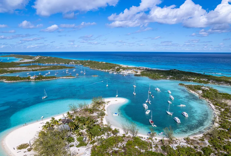 Aerial of a sandbar beach and busy turquoise anchorage filled with sailboats