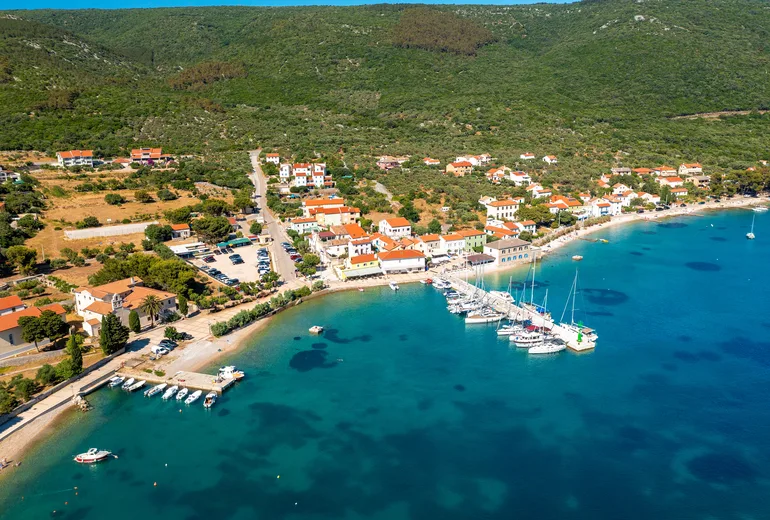 Aerial of a small harbour village with sailboats on the quay below wooded hills