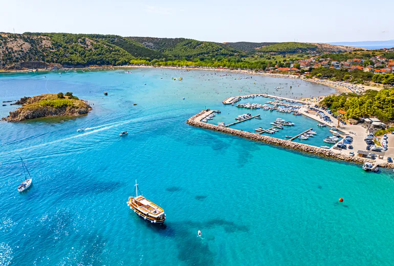 Aerial of a turquoise bay with an excursion boat, marina and busy beach, Croatia