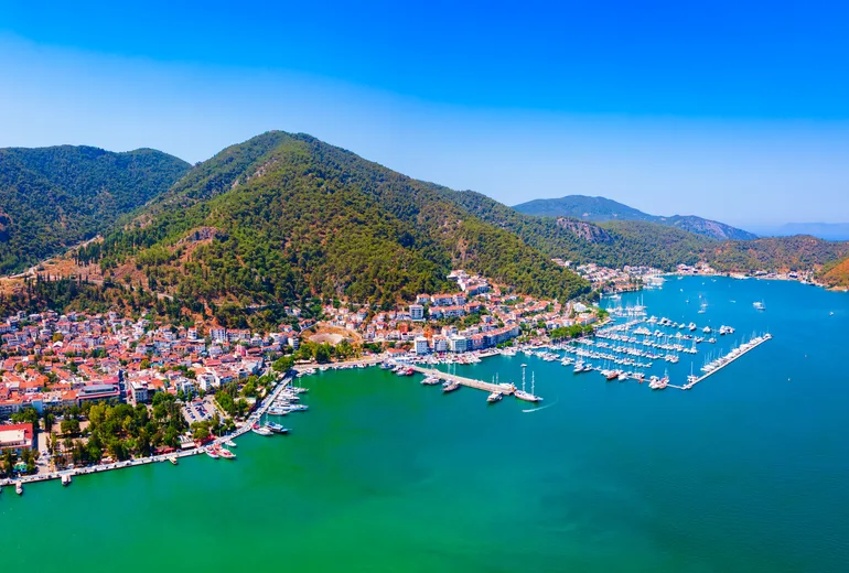 Aerial of Fethiye town and marina pontoons against forested mountain backdrop