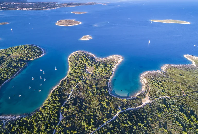 Aerial of green islets and coves dotted with a few anchored sailboats in northern Croatia