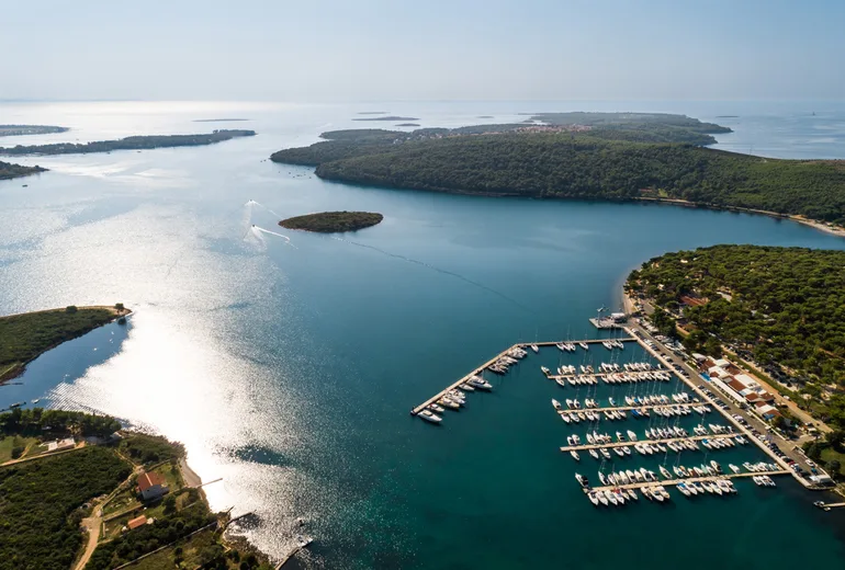 Aerial of Marina Pomer docks against a silvery backlit sea, Medulin bay, Croatia