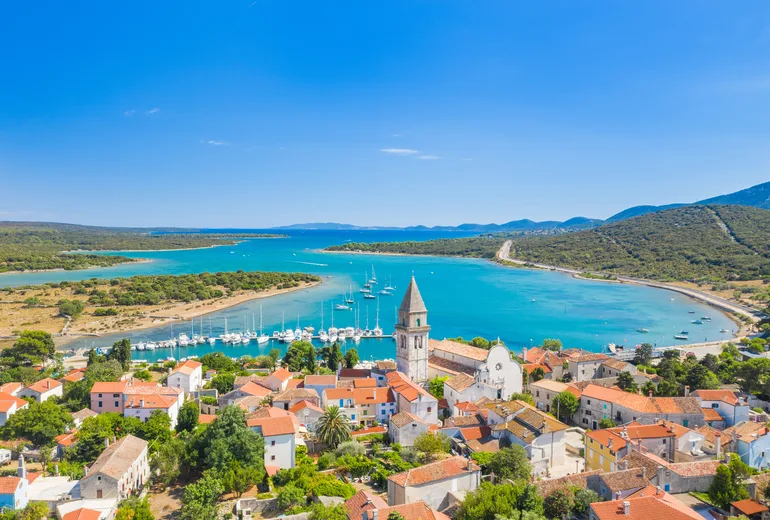 Aerial of Osor bell tower and town with sailboats moored in a turquoise bay, Croatia