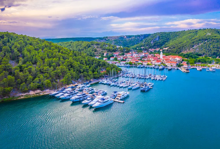 Aerial of Skradin riverside marina with moored yachts below a hilltop village at dusk, Croatia