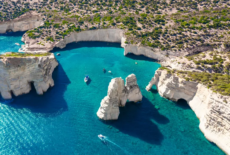 Aerial of the Kleftiko rock formations and boats in turquoise water, Milos, Greece