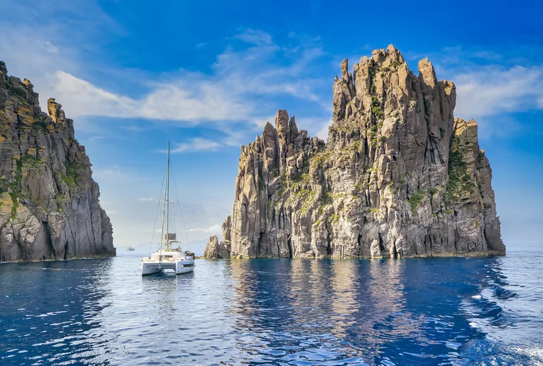 Catamaran anchored beside volcanic sea stacks in the Aeolian Islands