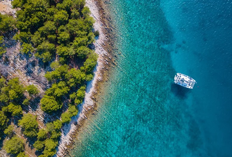 Catamaran anchored in clear turquoise water seen from above