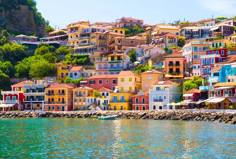 Colourful tiered houses of Parga rising above green harbour water in the Greek Ionian