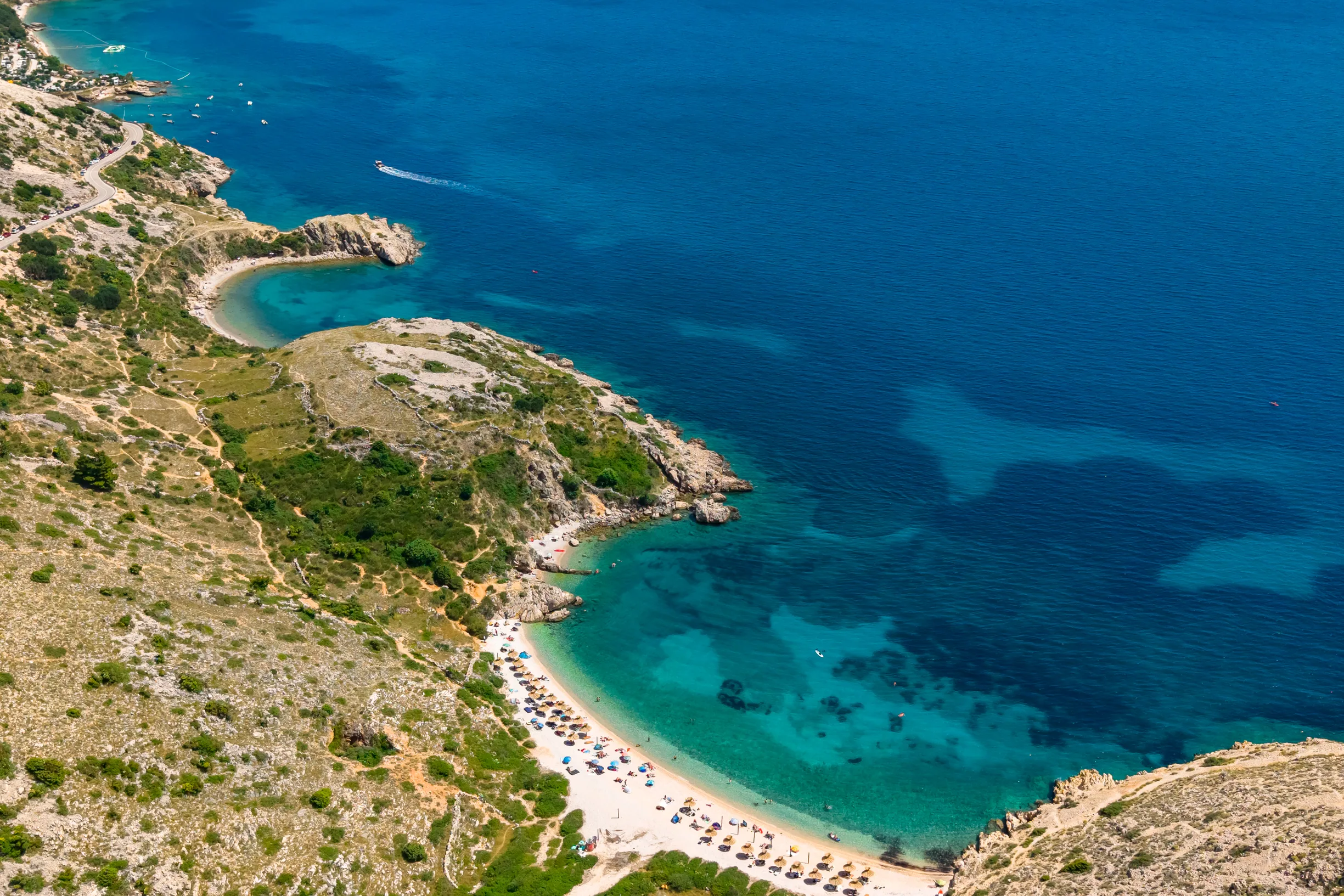 Vertical aerial of barren rocky coastline with busy pebble beach cove