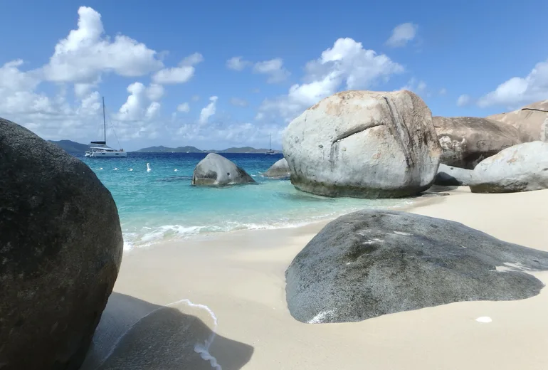 Granite boulders of The Baths, Virgin Gorda, with a catamaran anchored offshore, BVI
