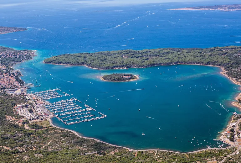 High aerial of Punat bay on Krk island with a large marina and a wooded islet, Croatia