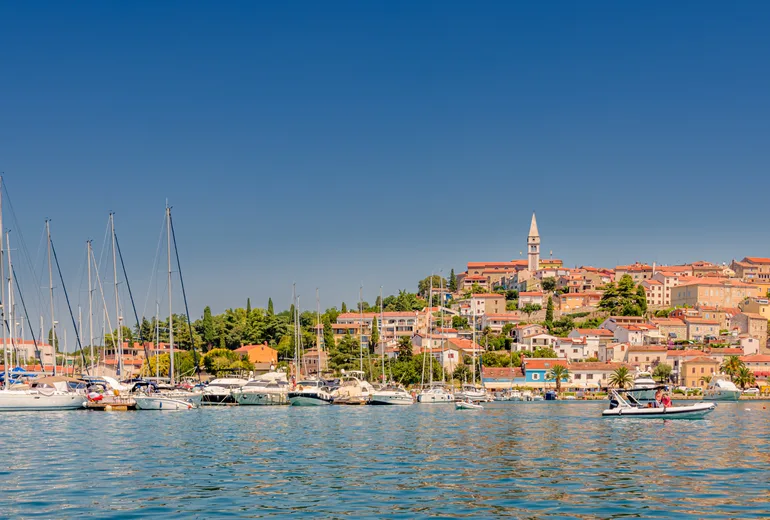 Hilltop coastal town with a bell tower above a sailboat-filled marina