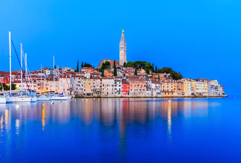 Rovinj old town and moored sailboats reflected in calm sea at blue hour, Croatia