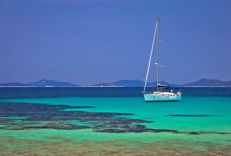 Sailboat anchored in turquoise shallows with low islands behind in Croatia