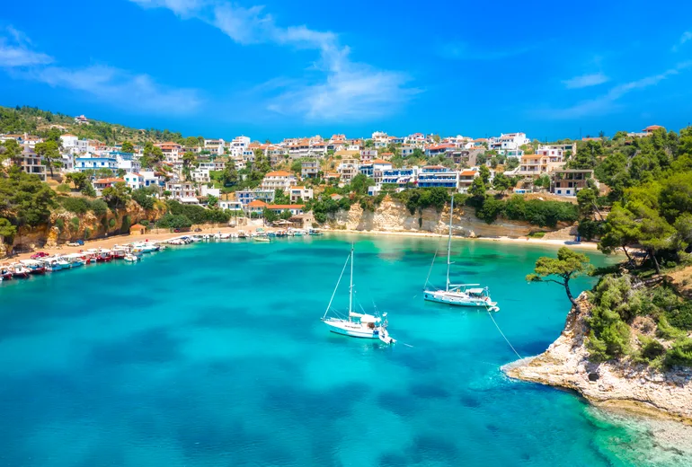 Sailboats moored in a turquoise cove below village houses on Alonissos, Sporades