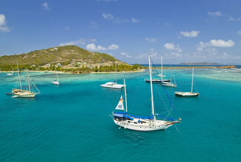 Sailing yachts anchored in a turquoise reef lagoon off a palm-fringed Caribbean island