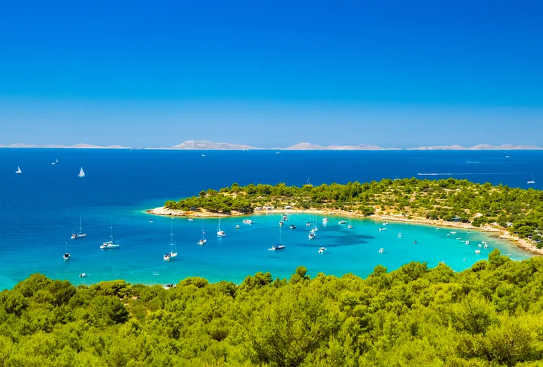 Turquoise bay anchorage with yachts, pine shores and distant islands in Croatia