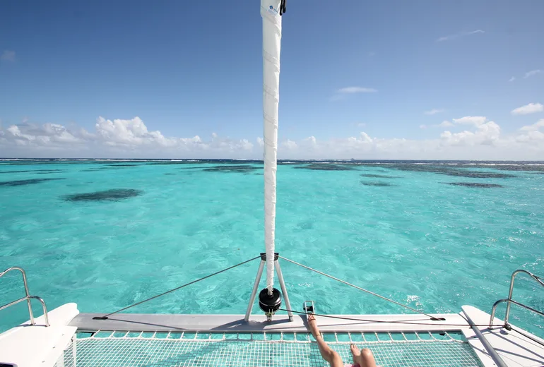 View from a catamaran bow trampoline over turquoise reef-dappled shallows