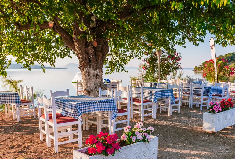 Waterside taverna tables shaded by an old tree at dusk