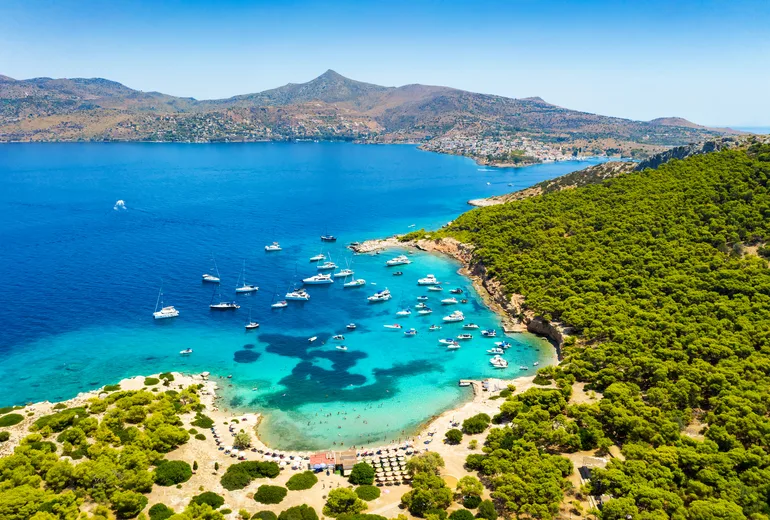 Yachts anchored off a pine-fringed islet beach in Greece
